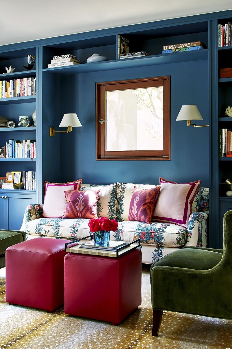 hình ảnh phòng khách nhỏ với tường sơn màu xanh dương, ghế bành xanh lá, bàn trà là ghế Ottoman màu hồng, sofa bọc vải hoa hút mắt
