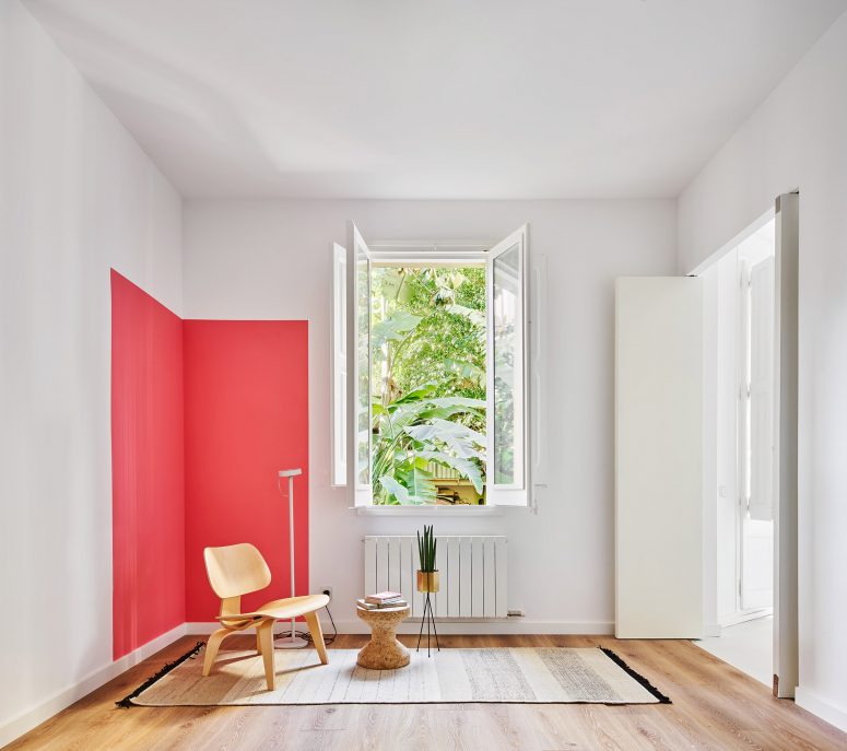 hình ảnh phòng khách nhỏ thoáng sáng với ghế gỗ nhỏ, thảm trải, cây xanh trang trí, cửa sổ kính, mảng tườn sơn màu đỏ cam nổi bật