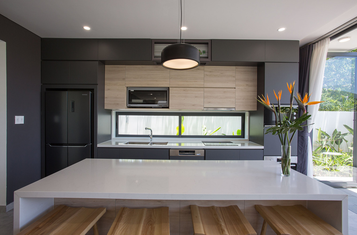 hình ảnh phòng bếp hiện đại với tủ màu xám đen xen kẽ chất liệu gỗ ấm áp, bàn đảo màu trắng, gầm bàn đặt ghế gỗ