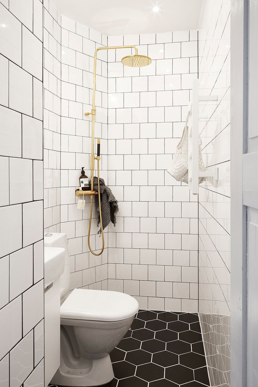 hình ảnh phòng tắm nhỏ với gạch ốp tường màu trắng, gạch nền màu đen, vòi tắm hoa sen bằng đồng sáng bóng