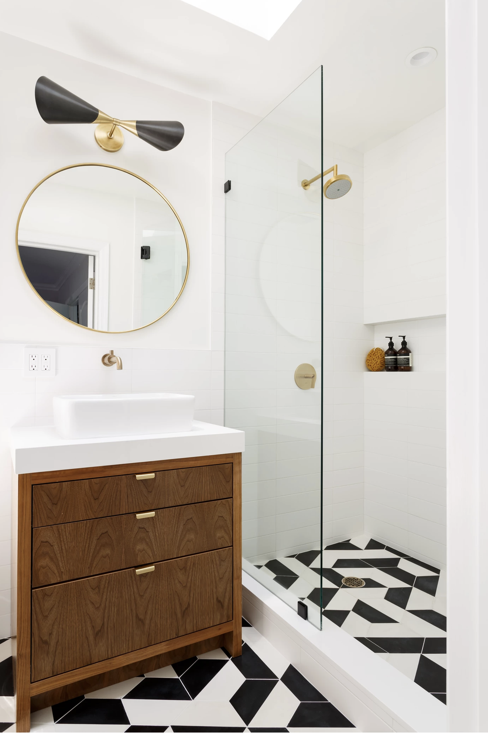 hình ảnh phòng tắm nhỏ màu trắng chủ đạo với gương tròn treo tường, đèn thắp sáng, vách kính phân tách với buồng tắm đứng