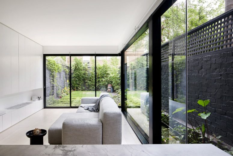 hình ảnh phòng khách phong cách tối giản với sofa ghi sáng, tủ kệ màu trắng âm tường, tường và cửa kính trong suốt mở ra sân vườn