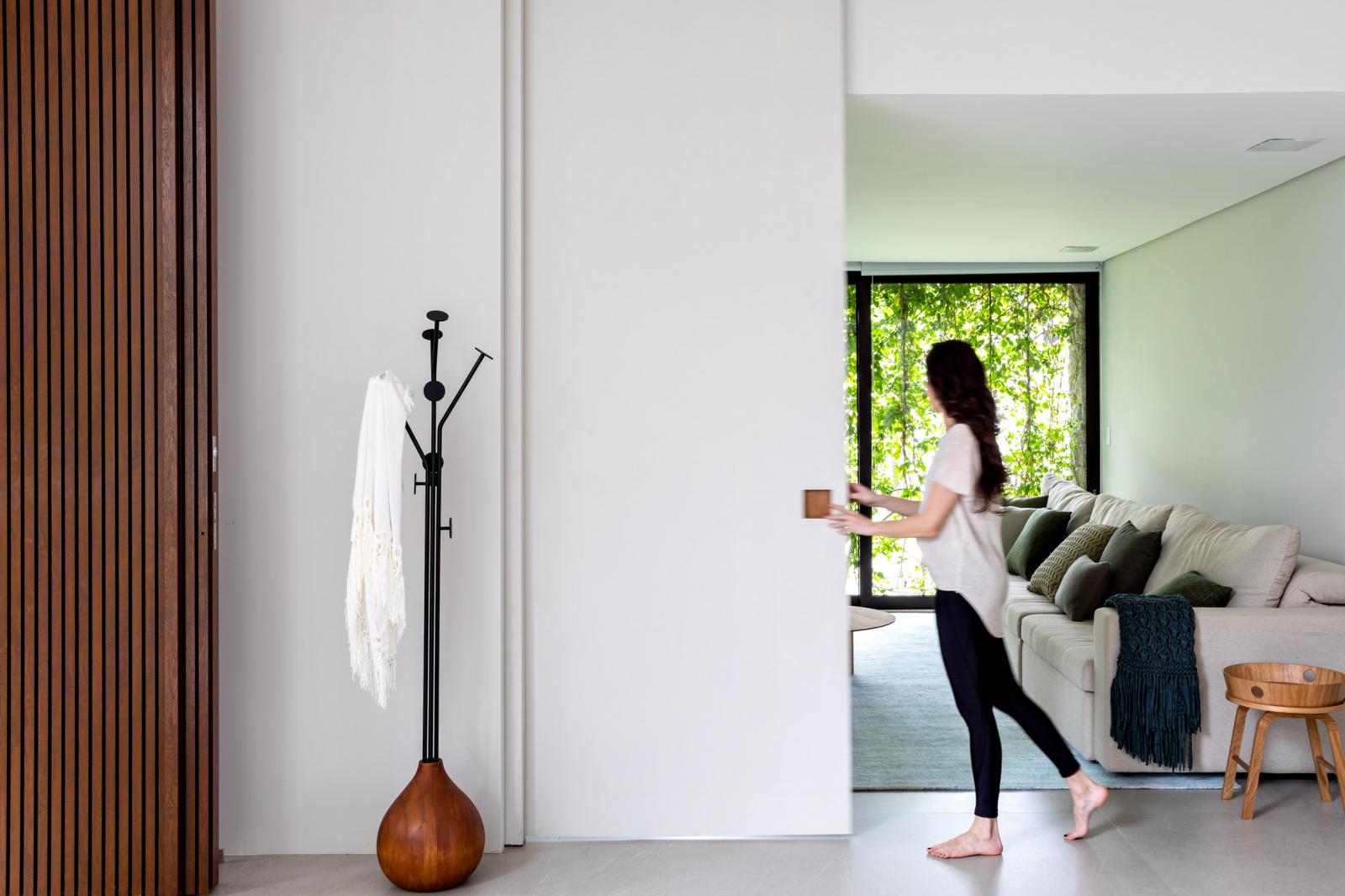 hình ảnh cô gái trẻ đứng ở hành lang ngôi nhà tối giản, cạnh đó là phòng khách, tường ốp gỗ, phụ kiện trang trí