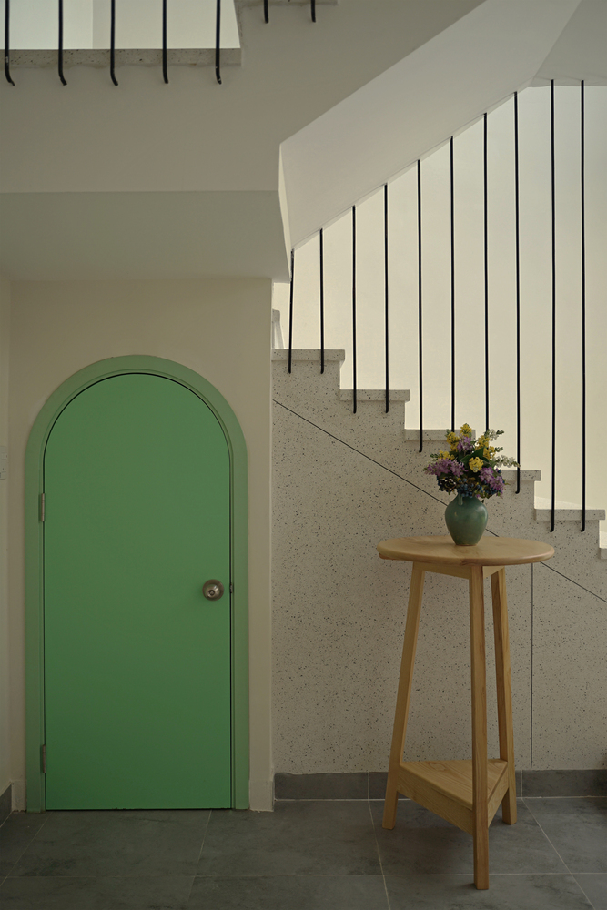 hình ảnh cầu thang dẫn lên tàng trên nhà ống, cánh cửa sơn xanh lá, kệ gỗ để bình hoa tươi