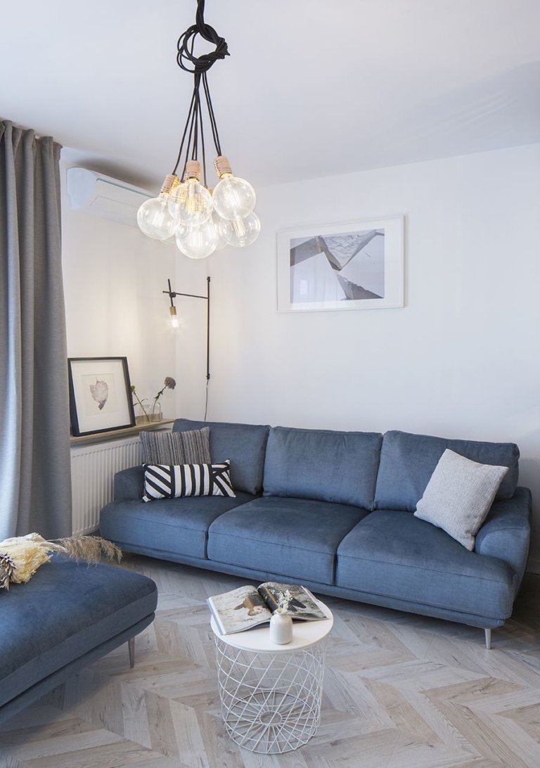 hình ảnh phòng khách nhỏ xinh với gối sofa xanh, gối tựa kẻ sọc, đèn chùm, bàn trà màu trắng tròn