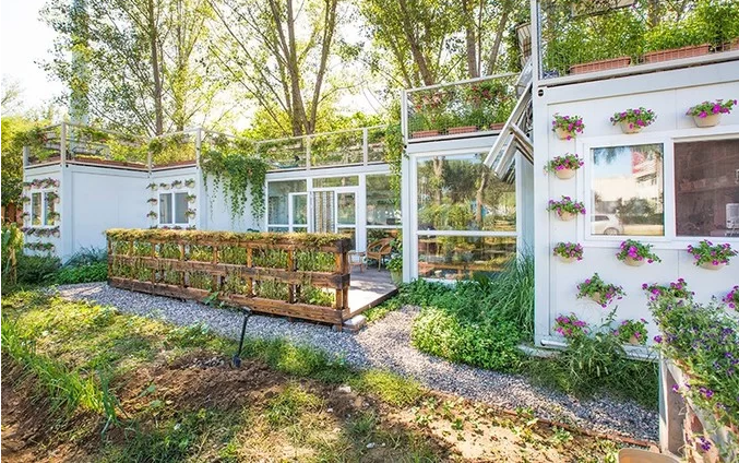 hình ảnh cận cảnh mặt tiền ngôi nhà container màu trắng xinh xắn người chồng tặng vợ, xung quanh là vườn cây xanh tốt