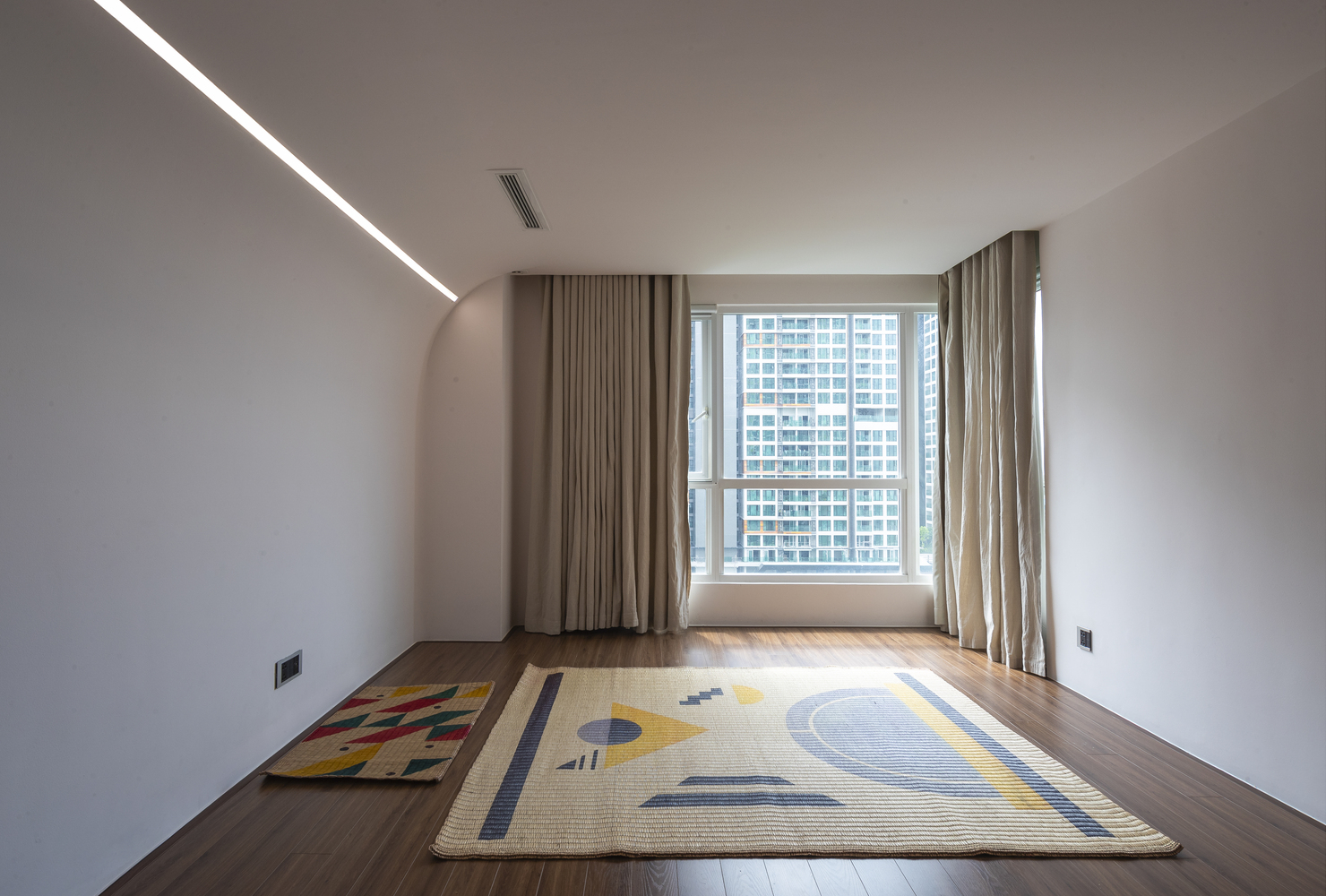 hình ảnh căn phòng rộng rãi, thoáng sáng trong căn hộ đương đại với chiếu trải, thảm màu sắc, khung cửa kính lớn, rèm cửa hai lớp