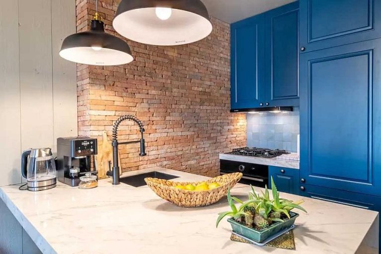 hình ảnh phòng bếp căn hộ hiện đại với bức tường gạch lộ, tủ sơn xanh dương, đèn thả với phần chụp màu đen