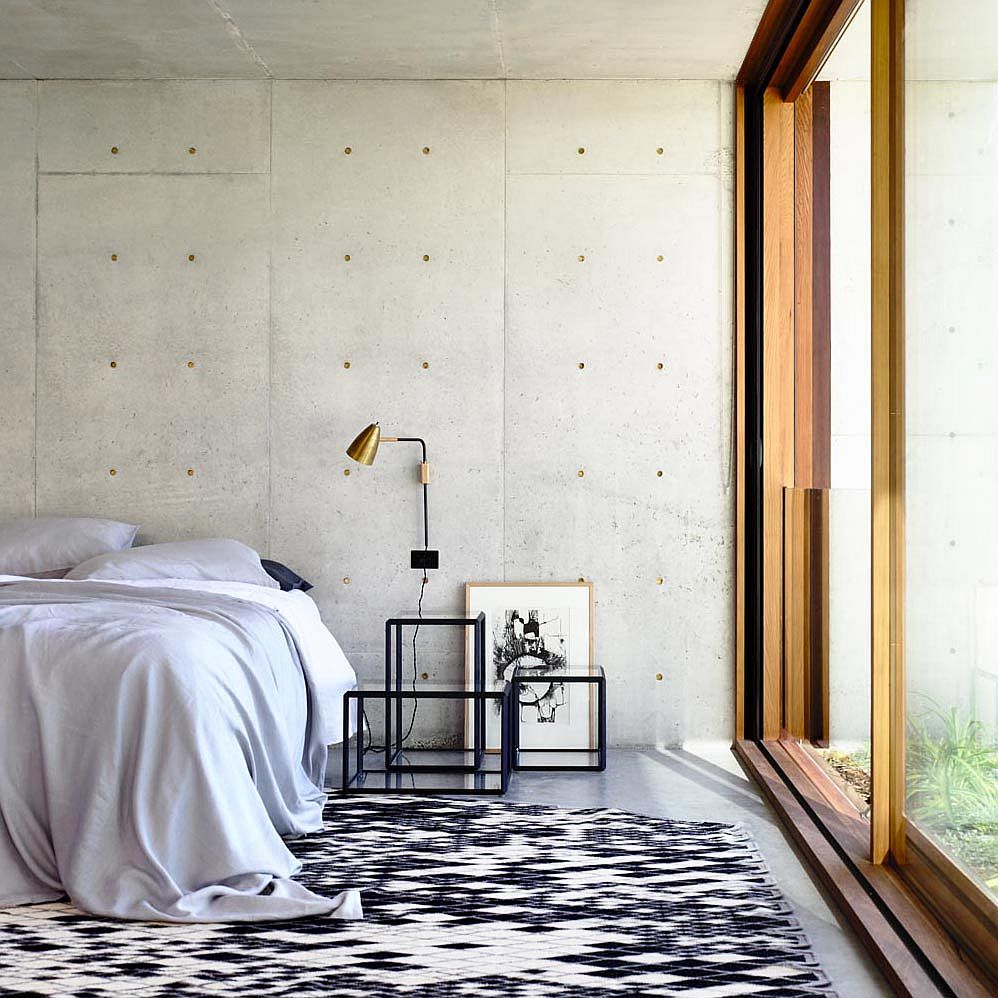 Những bức tường bê tông lộ ra ngoài tạo ra một bối cảnh tối giản hiện đại trong phòng ngủ với cửa kính trượt ngập tràn ánh sáng.
