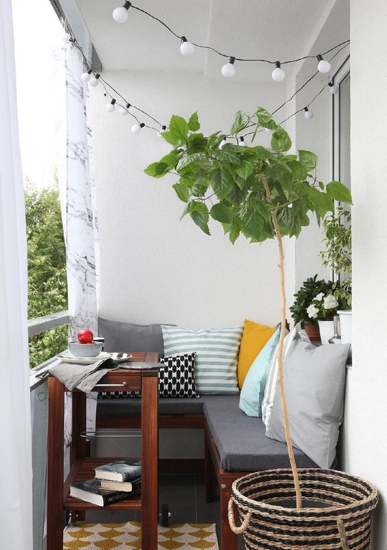 Một ban công nhỏ ấm cúng với ghế chữ L bọc nệm màu xám, bàn cà phê nhỏ và những chậu cảnh xanh mướt tạo điểm nhấn.