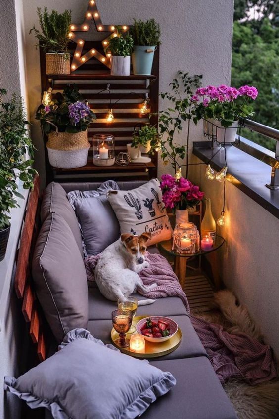 Một ban công nhỏ ấm áp với bức tường ốp gỗ pallet, ghế sofa êm ái kết hợp hài hòa với chậu hoa, cây xanh và đèn nến.
