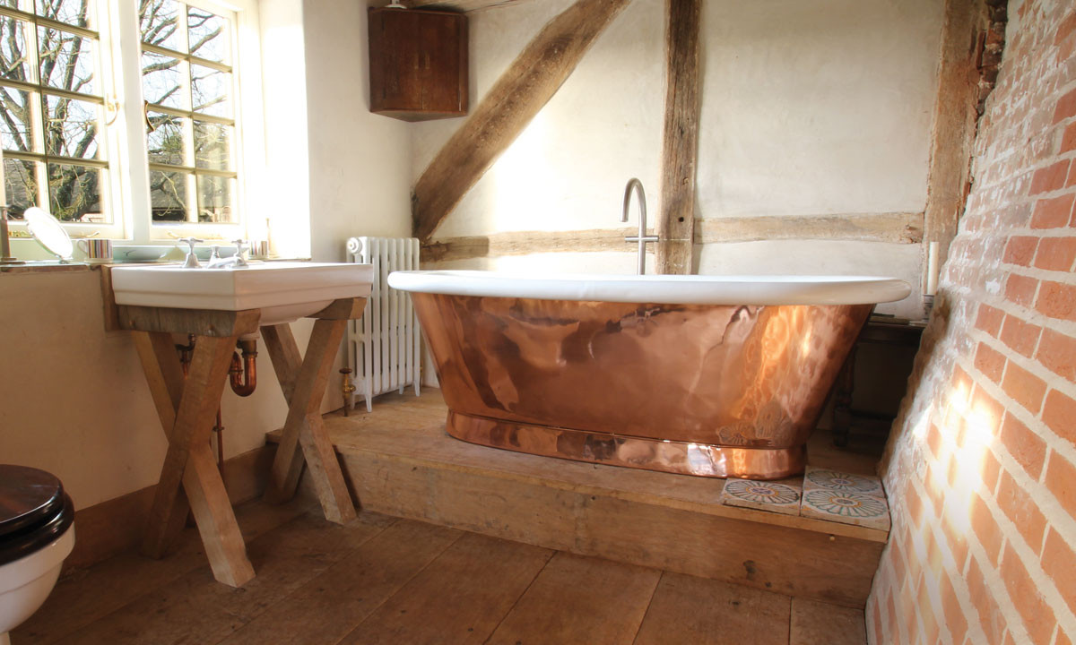 bồn tắm bằng đồng thô mộc trong phòng tắm sử dụng gạch trần, gỗ nguyên bản
