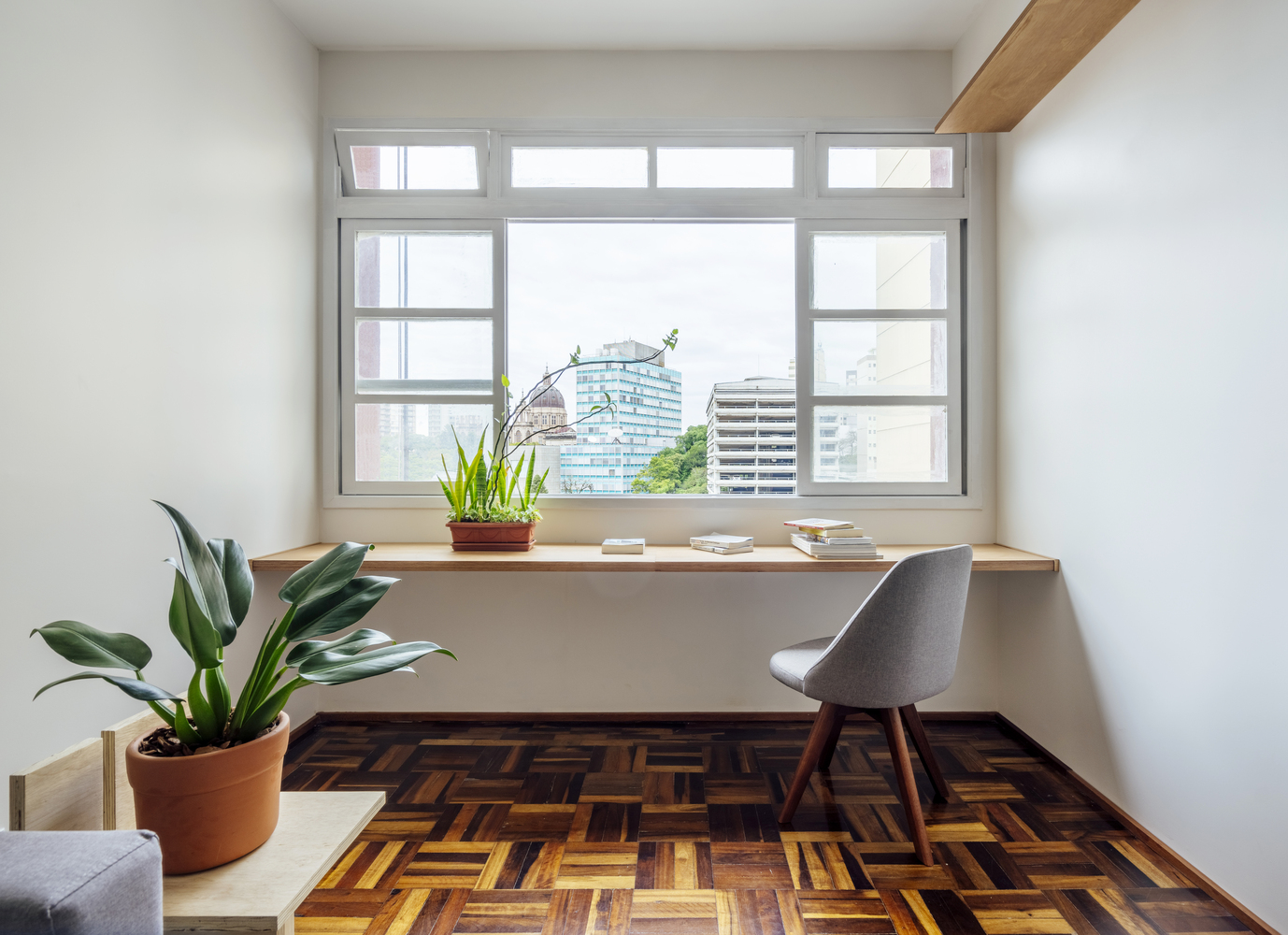 Góc làm việc thoáng sáng cạnh cửa sổ phòng khách với thiết kế đơn giản gồm phản gỗ gắn tường, ghế tựa gọn xinh và chậu cây xanh trang trí.