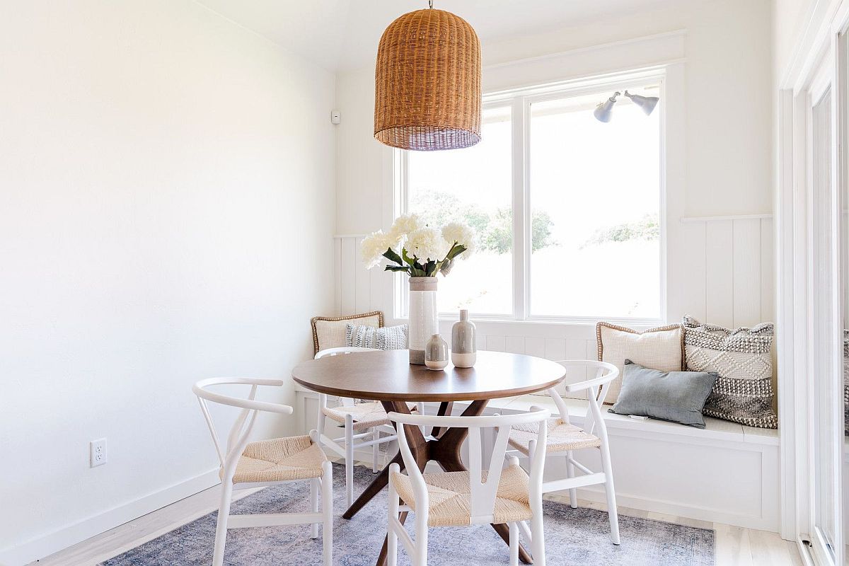 Phòng ăn nhỏ màu trắng ngập tràn ánh sáng với bàn ăn tròn và góc thư giãn thoải mái bên khung cửa kính trong suốt.
