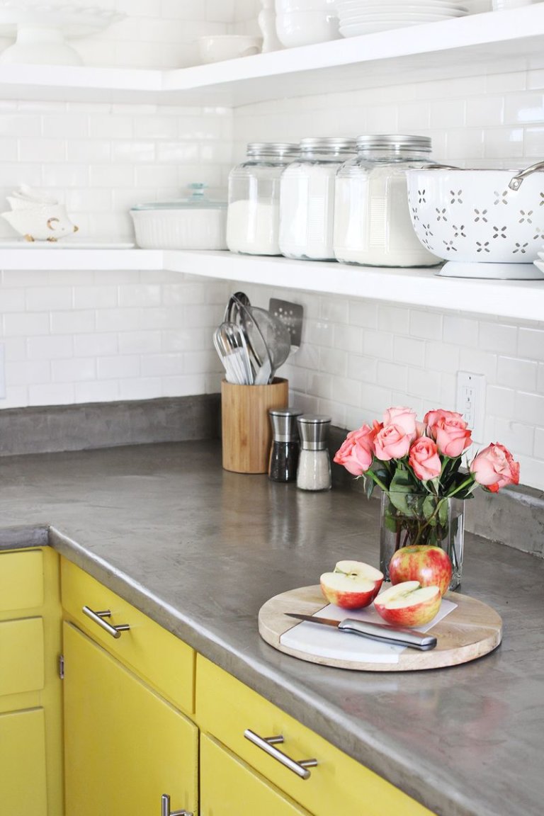 Bề mặt bàn bếp bê tông tự làm tạo ấn tượng thị giác mạnh mẽ khi tương phản với hệ tủ lưu trữ sơn màu vàng chanh tươi sáng.