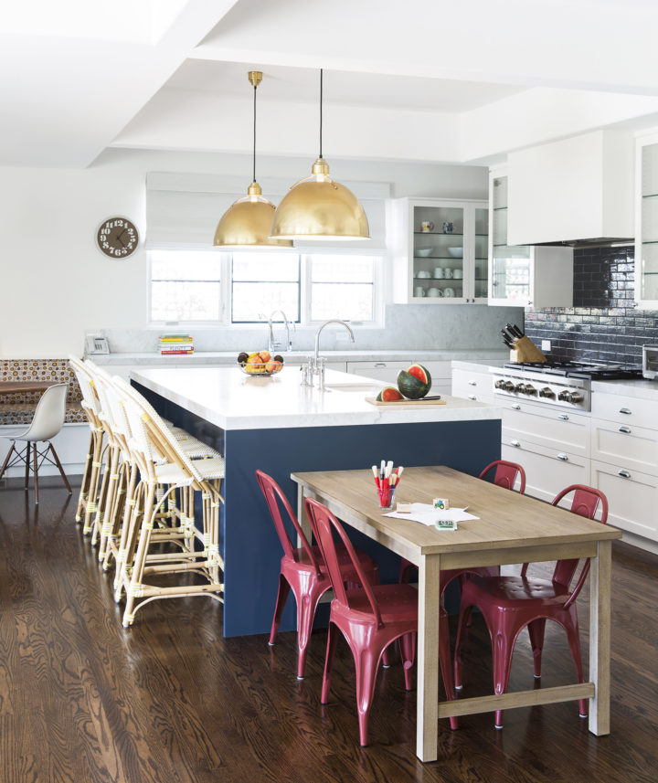 phòng bếp hiện đại với đảo bếp màu trắng, cạnh đó là bàn gỗ, ghế đỏ dành cho trẻ