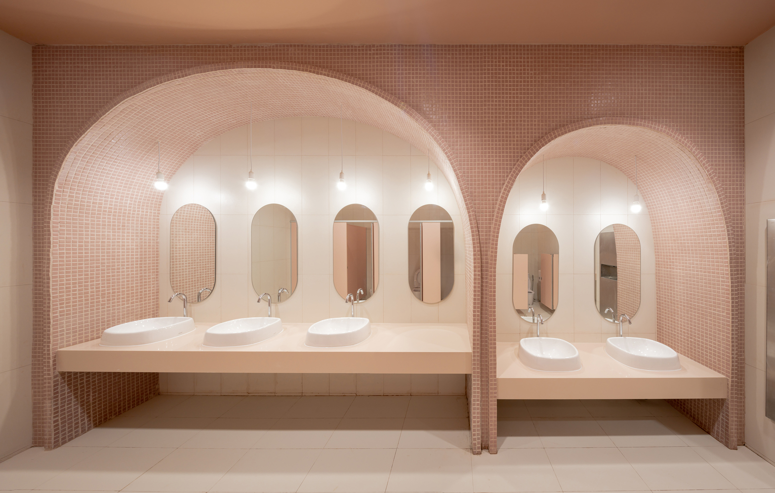 nhà vệ sinh với kiến trúc hình vòm, tường ốp gạch chỉ màu hồng đất, gương bầu dục, bồn rửa sứ trắng