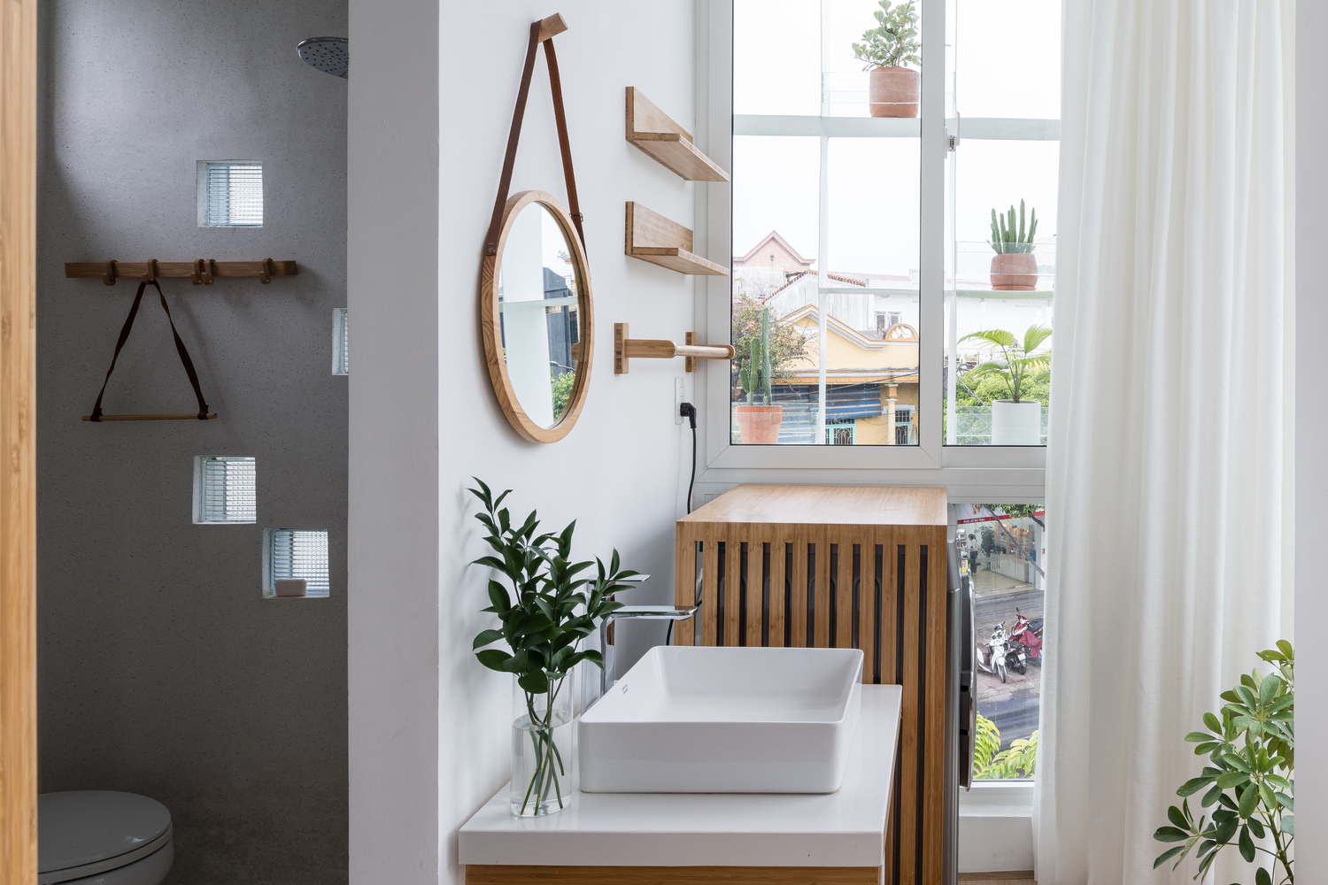 góc phòng vệ sinh hiện đại với gương tròn khung gỗ, bệ rửa gỗ, cửa sổ kính ngập tràn ánh sáng tự nhiên