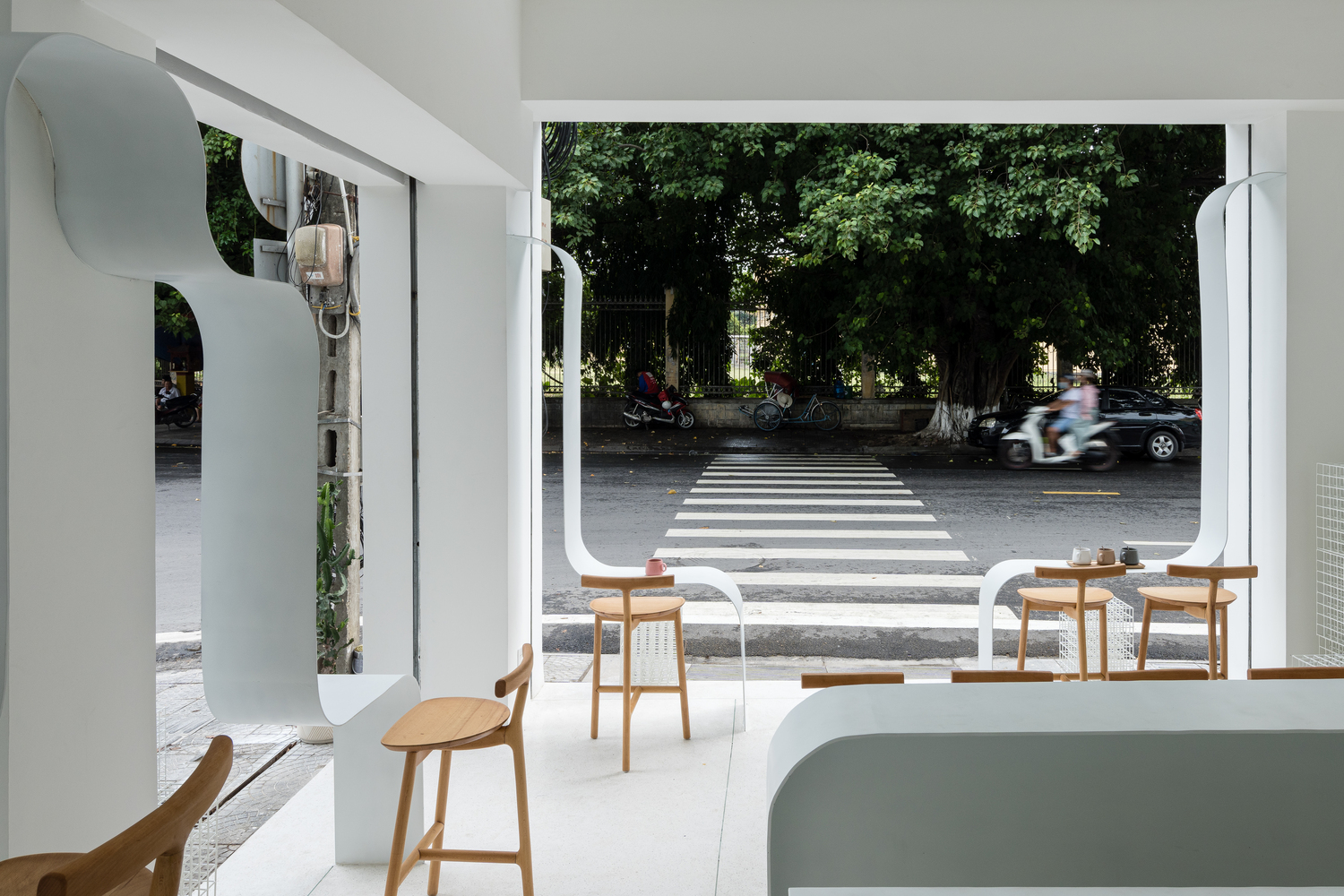 tầng trệt quán cà phê với ghế ngồi bằng gỗ cao thoáng, nhìn ra đường lớn với nhiều cây xanh