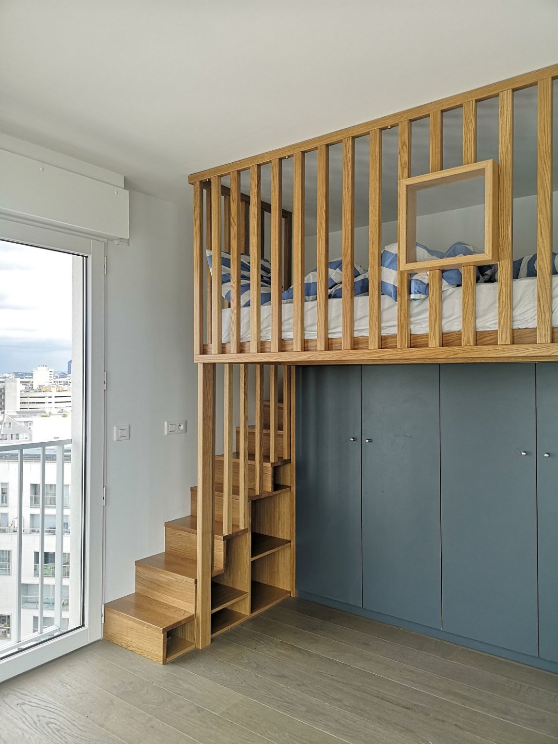 giường tầng với cầu thang gỗ đi lên, dưới giường là tủ quần áo màu xám