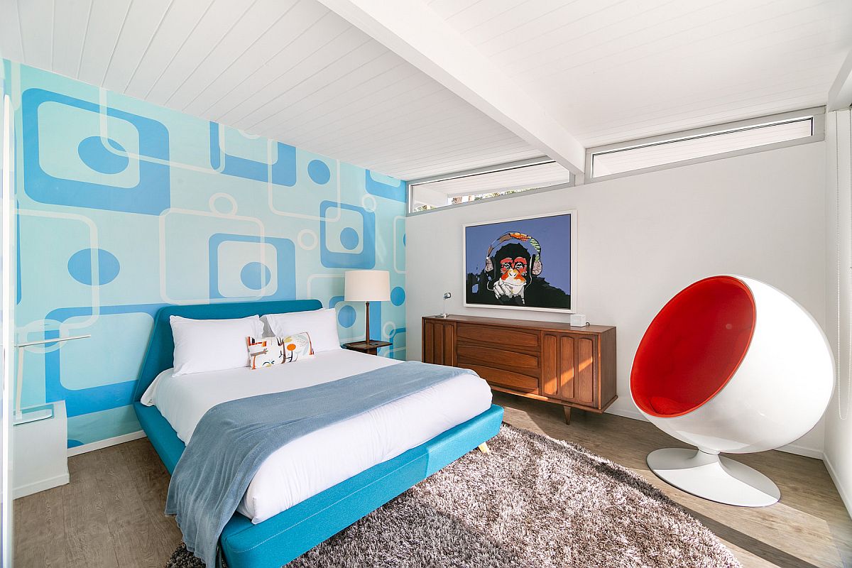 phòng ngủ trẻ em với giường màu xanh dương cùng tông với giấy dán tường đầu giường, ghế quả trứng màu đỏ - trắng, tủ ngăn kéo gỗ