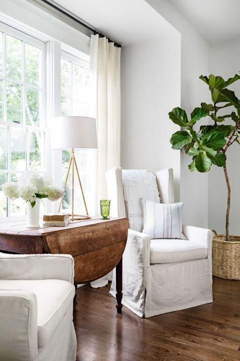 hình ảnh bàn gỗ màu nâu và hai ghế bành lớn màu trắng, êm ái đặt cạnh cửa sổ kính phòng khách.
