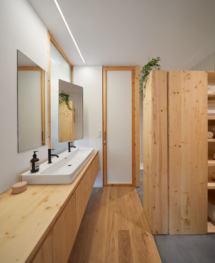 phòng tắm với vật liệu gỗ màu sáng, 2 gương gắn tường, bồn rửa mặt dài, vòi nước màu đen