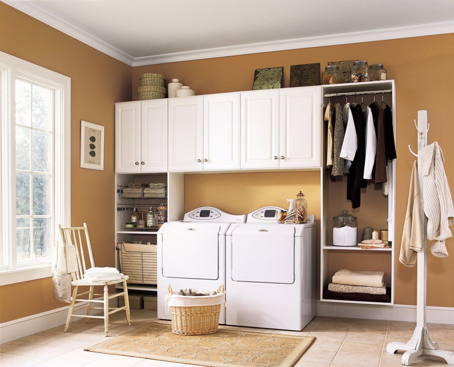 hình ảnh phòng giặt với nền tường sơn màu vàng gạch, nổi bật là hệ tủ kệ gắn tường màu trắng, phía dưới là thanh treo, hộc tủ âm tường gấp quần áo