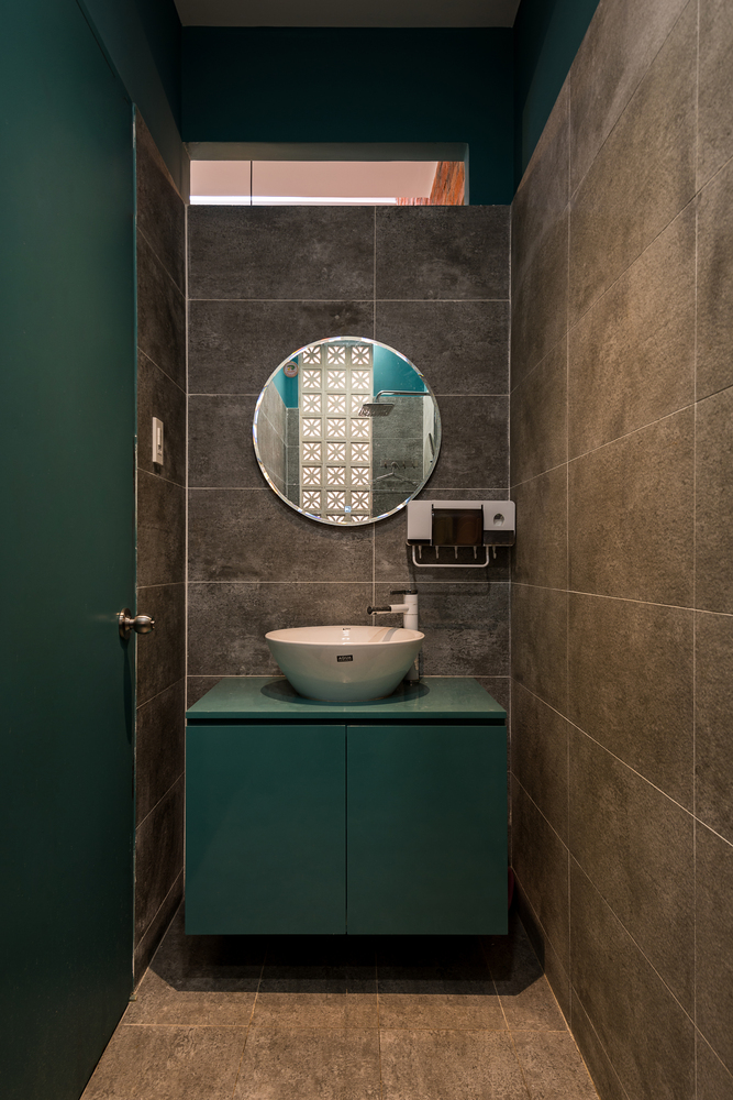 hình ảnh phòng tắm nhỏ với tường sơn màu xanh lá, sàn lát gạch bê tông màu xám, gương tròn gắn tường