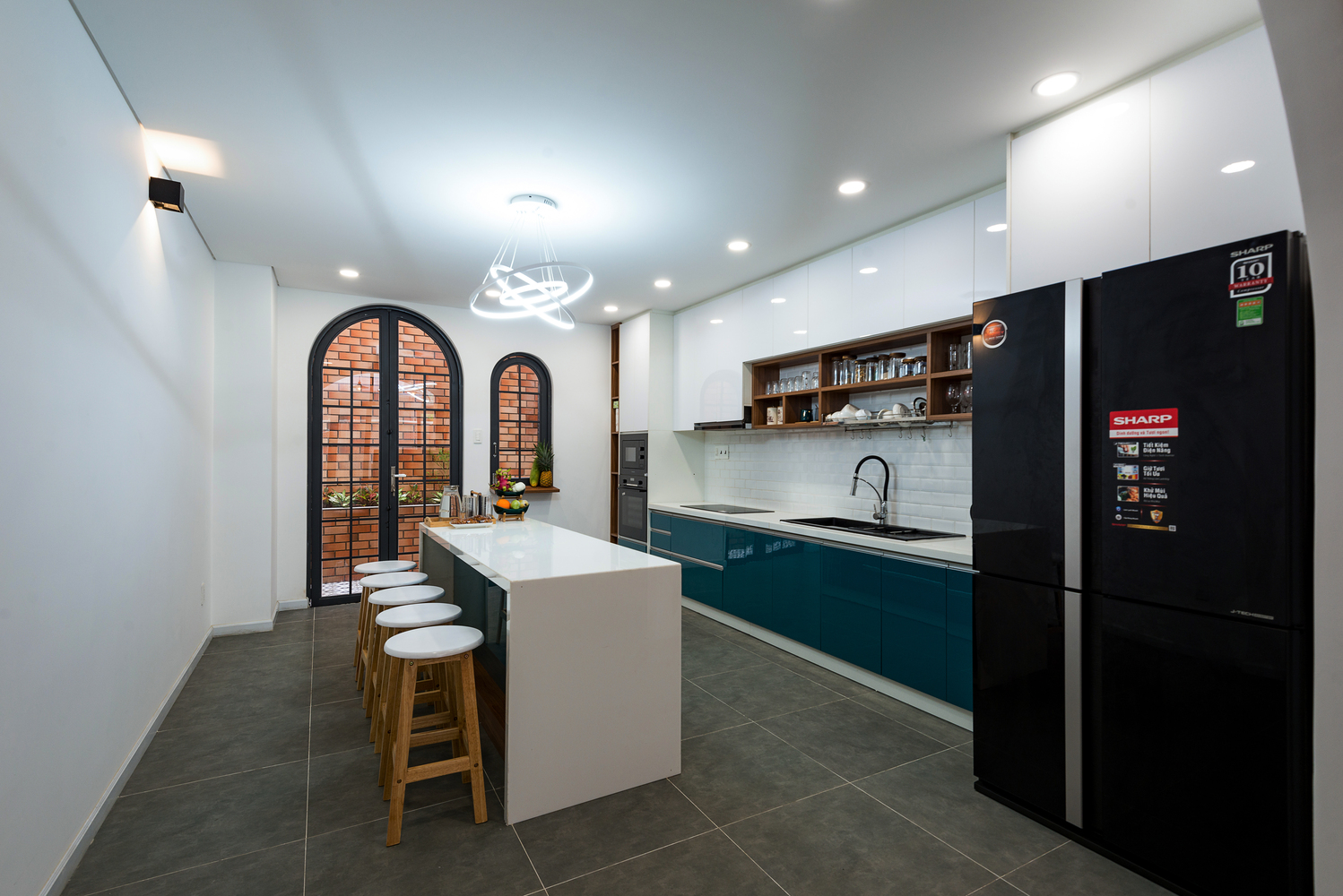 hình ảnh phòng bếp rộng rãi với tông màu trắng chủ đạo, điểm nhấn xanh ở tủ bếp dưới, bàn đảo trung tâm, tủ lạnh lớn màu đen