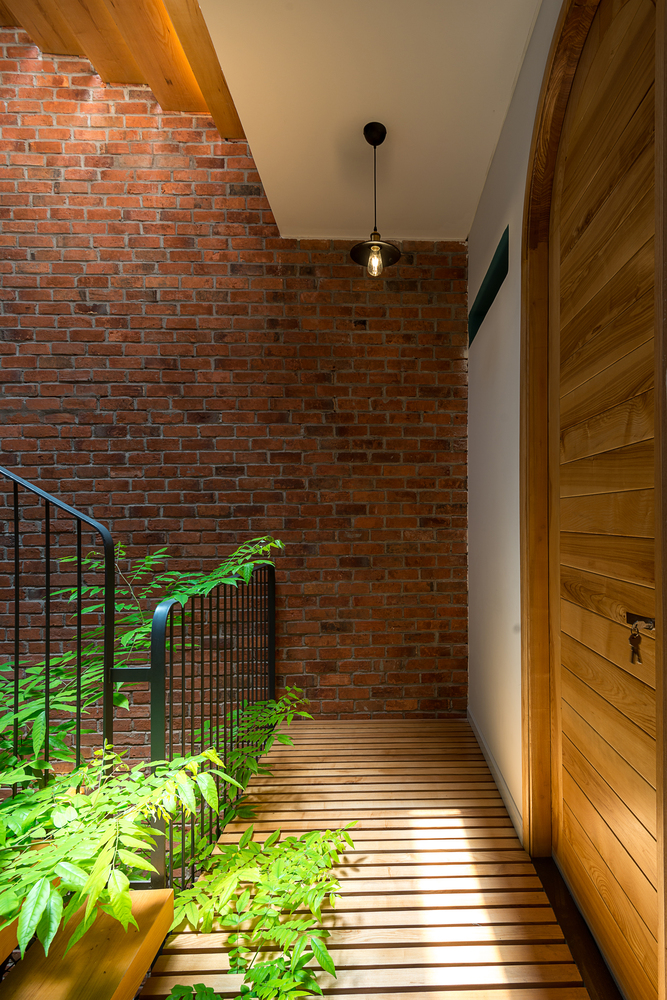 khu vực hành lang nhà phố 4 tầng với sàn lát gỗ màu sáng, tường gạch đỏ, cây xanh
