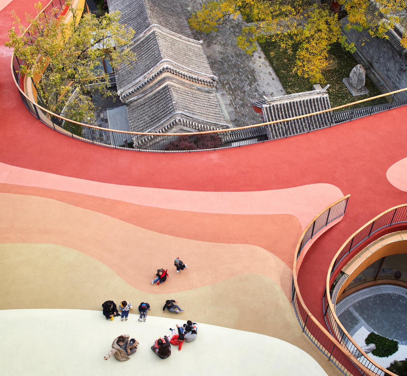 Trường mẫu giáo gây ấn tượng với phần mái màu đỏ và cam tươi bao phủ, tương phản với mái ngói màu xám cổ kính của các công trình lân cận.