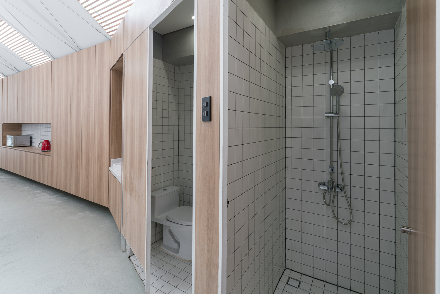 Phòng tắm, vệ sinh ốp lát gạch men màu trắng sạch sẽ được tích hợp trong  ​khối gỗ trung tâm.