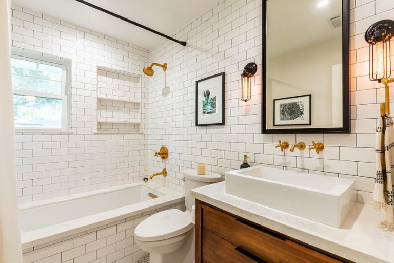 Phòng tắm với bồn tắm nằm, gạch ốp tường màu trắng, vòi nước mạ vàng sáng bóng.