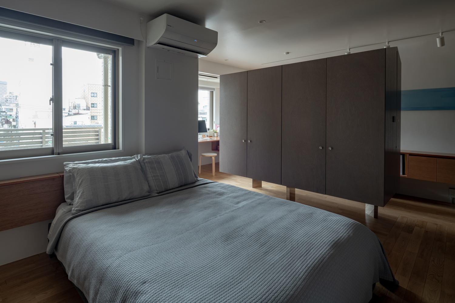 hình ảnh phòng ngủ đơn giản với tường sơn màu trắng sáng, ga gối màu xám, cửa sổ kính trong suốt, tủ quần áo lơ lửng