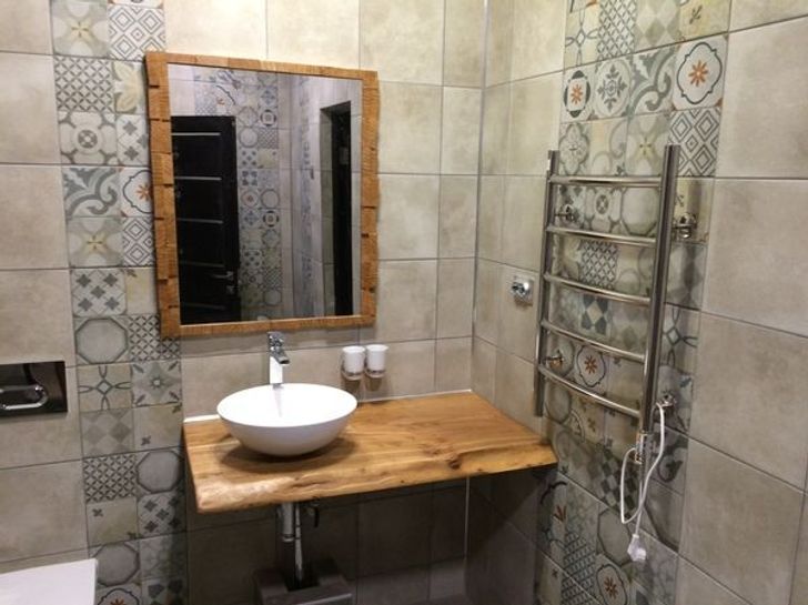 hình ảnh cận cảnh tường phòng tắm ốp gạch bông trang trí, khung gương và bề mặt bàn rửa bằng gỗ tự nhiên