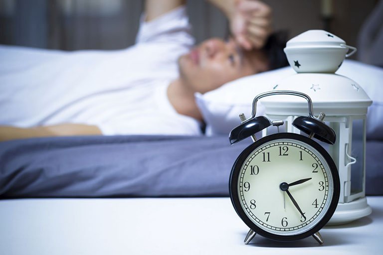 hình ảnh người đàn ông mặc áo trắng nằm trên giường, đồng hồ báo thức