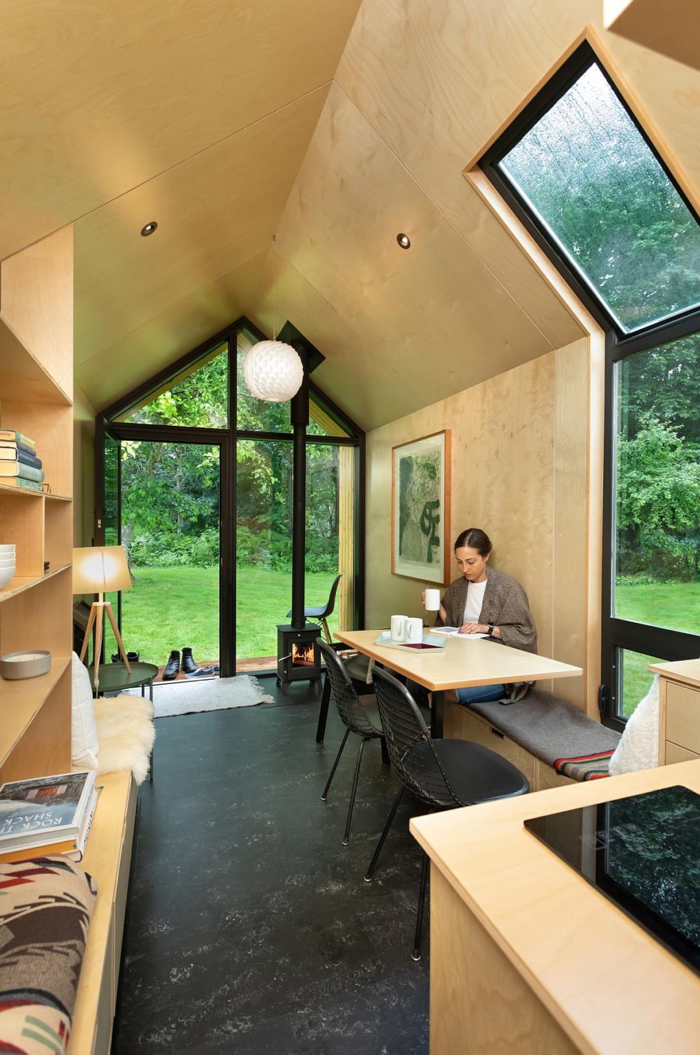 hình ảnh không gian bên trong nhà cabin với nội thất gỗ tuyết tùng màu sáng, người phụ nữ uống cà phê, làm việc