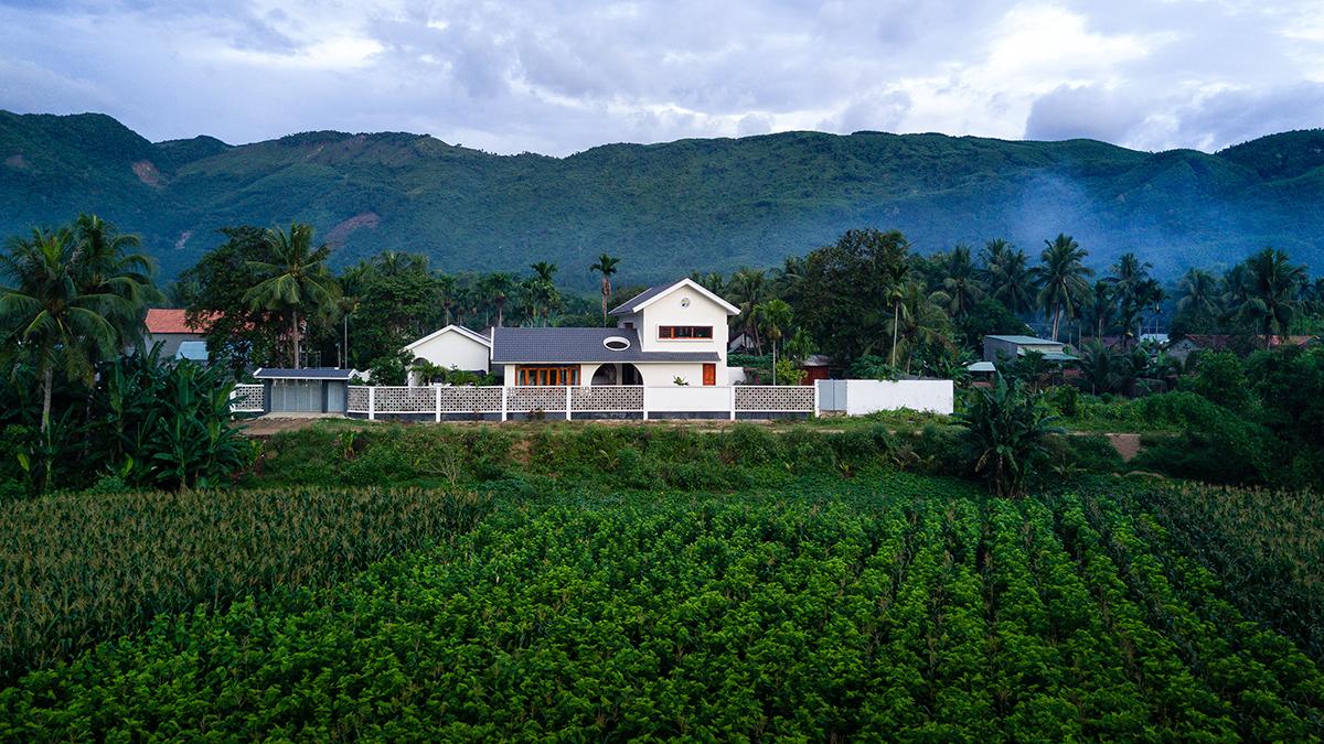 hình ảnh mẫu nhà cấp 4 mái Thái tọa lạc giữa vùng quê xanh mướt, bên sau là núi đồi, trước là đồng ruộng