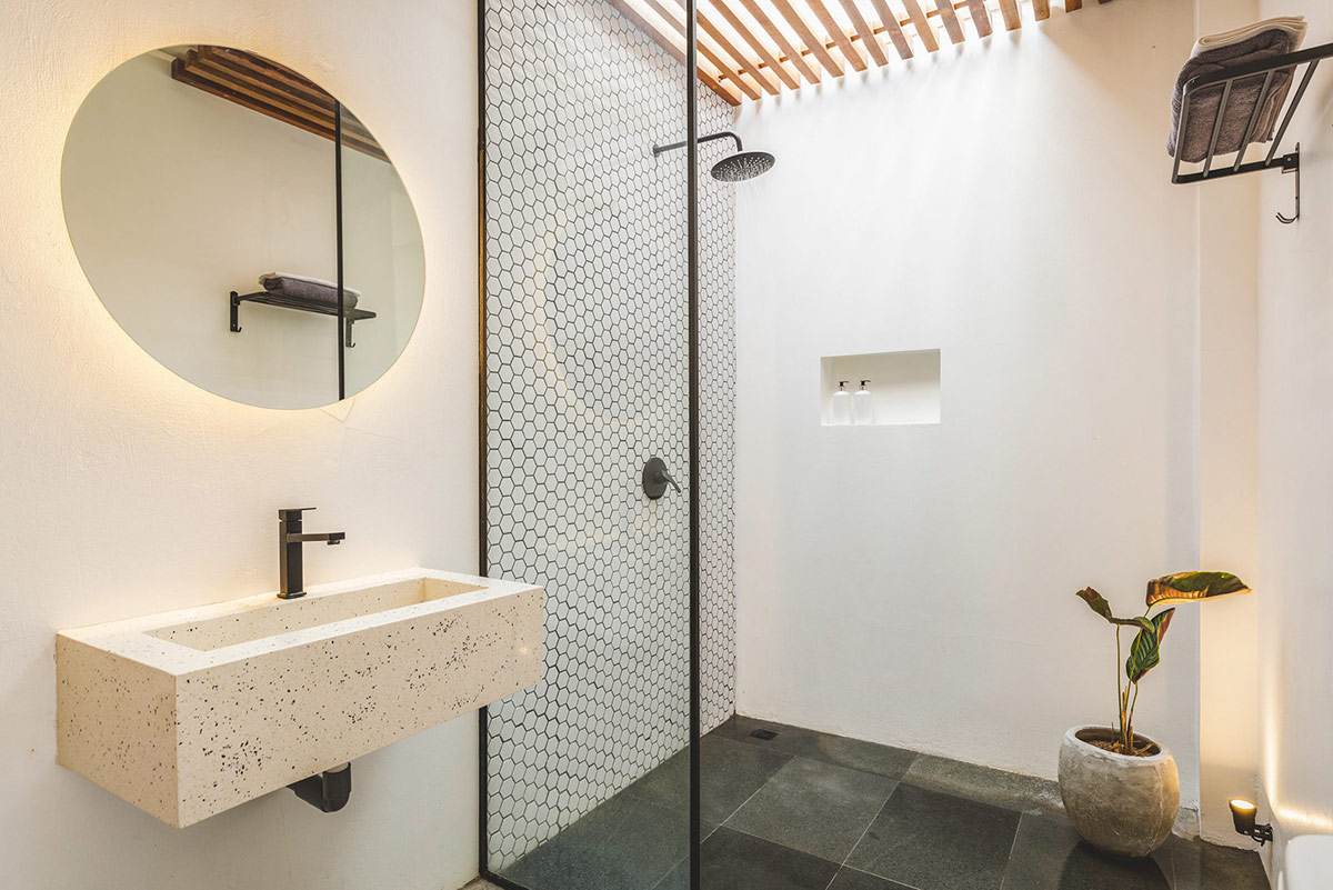 Phòng tắm lấy sáng tự nhiên từ hệ lam gỗ trên trần khu vực vòi hoa sen. Gạch lát màu xám đen giúp gia tăng chiều sâu cho căn phòng.