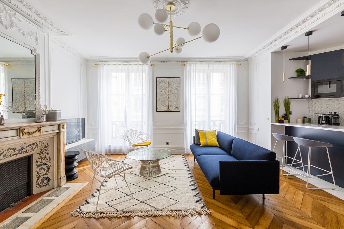 Phòng khách với tường và trần sơn màu trắng, sàn lát gỗ xương cá, ghế sofa màu xanh đậm