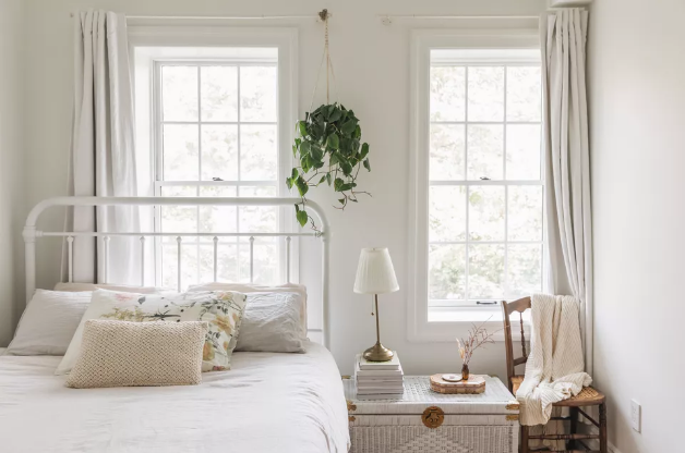 hình ảnh phòng ngủ tông màu trắng chủ đạo, đầu giường kê dưới cửa sổ, có rèm che, cây xanh trang trí