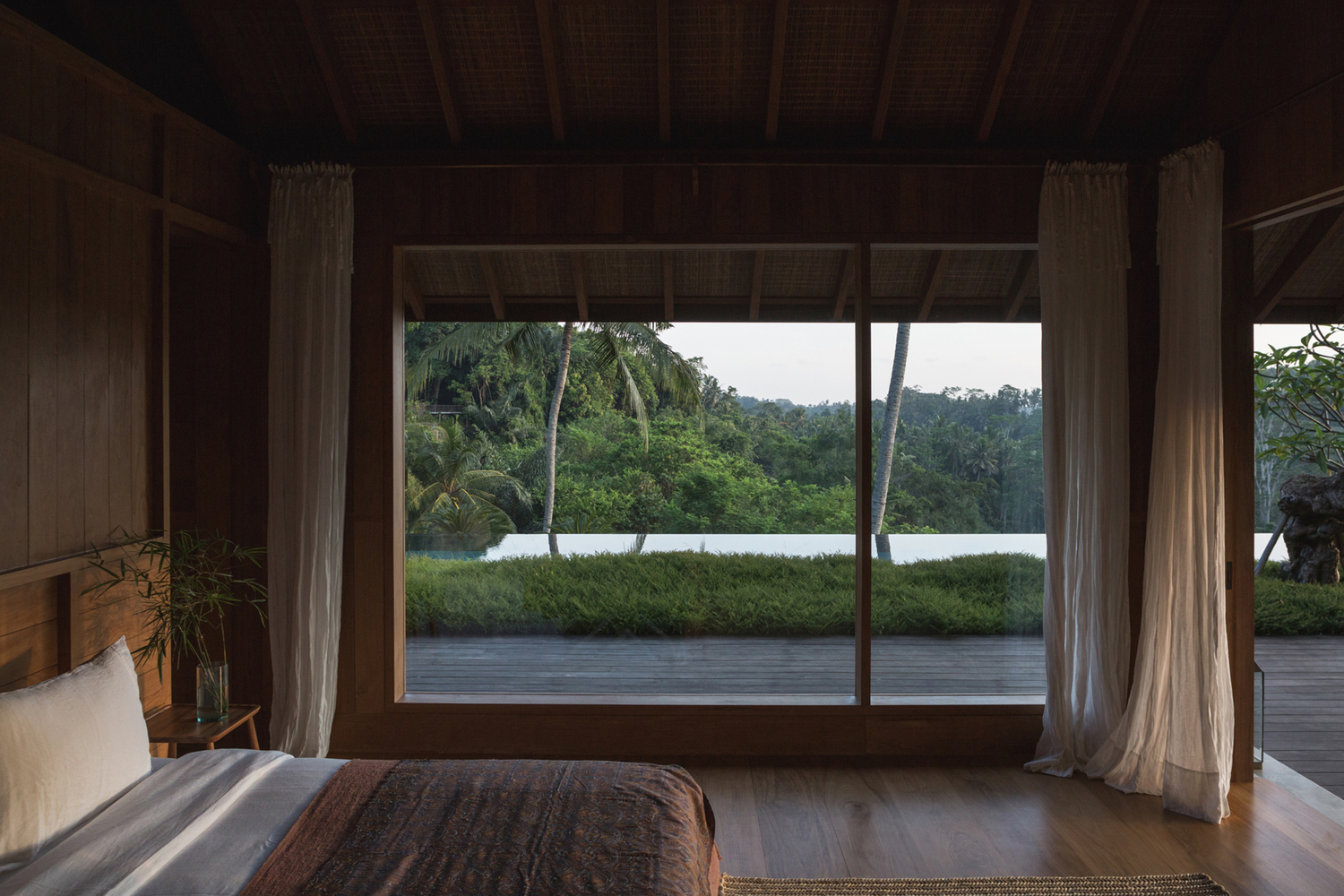 hình ảnh phòng ngủ với cửa kính lớn, rèm màu trắng, hướng nhìn ra khung cảnh núi rừng