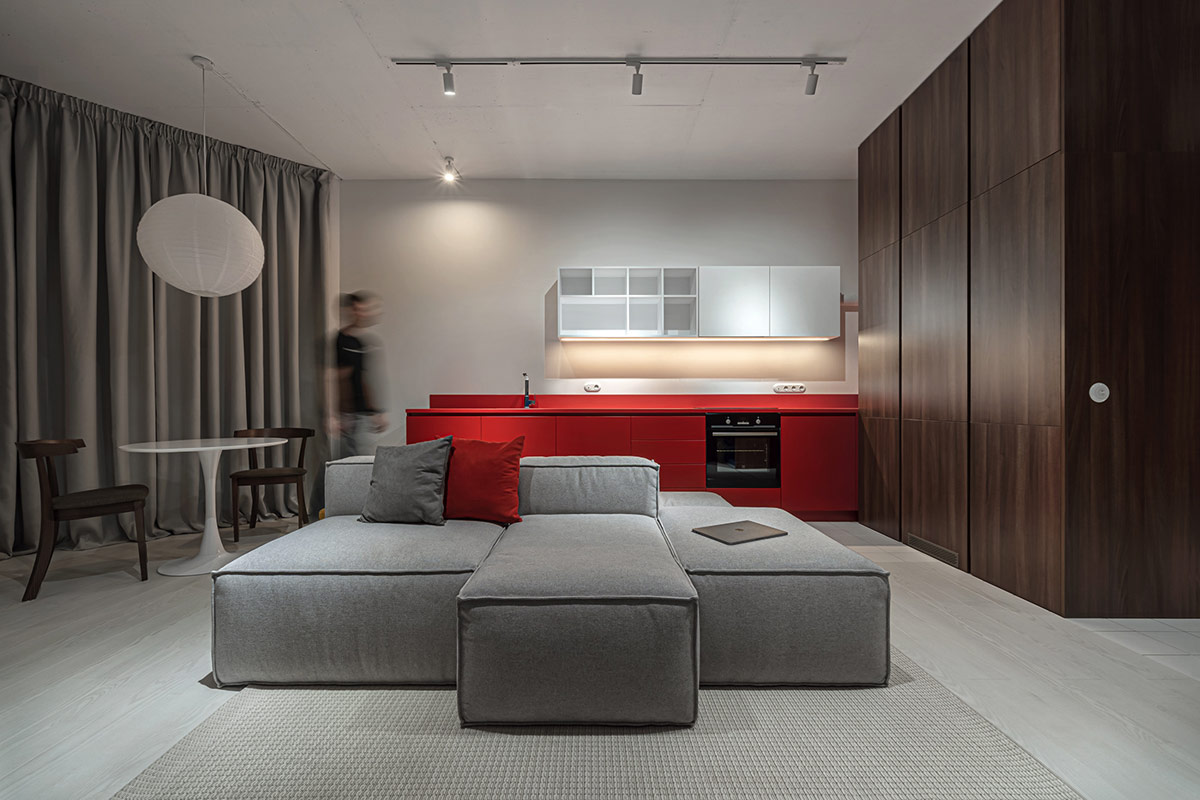 hình ảnh phòng khách căn hộ 52m2 với ghế sofa màu xám đặt ở trung tâm, gối tựa màu đỏ, kệ tivi màu đỏ, rèm cửa màu xám, đèn thả màu trắng hình tròn