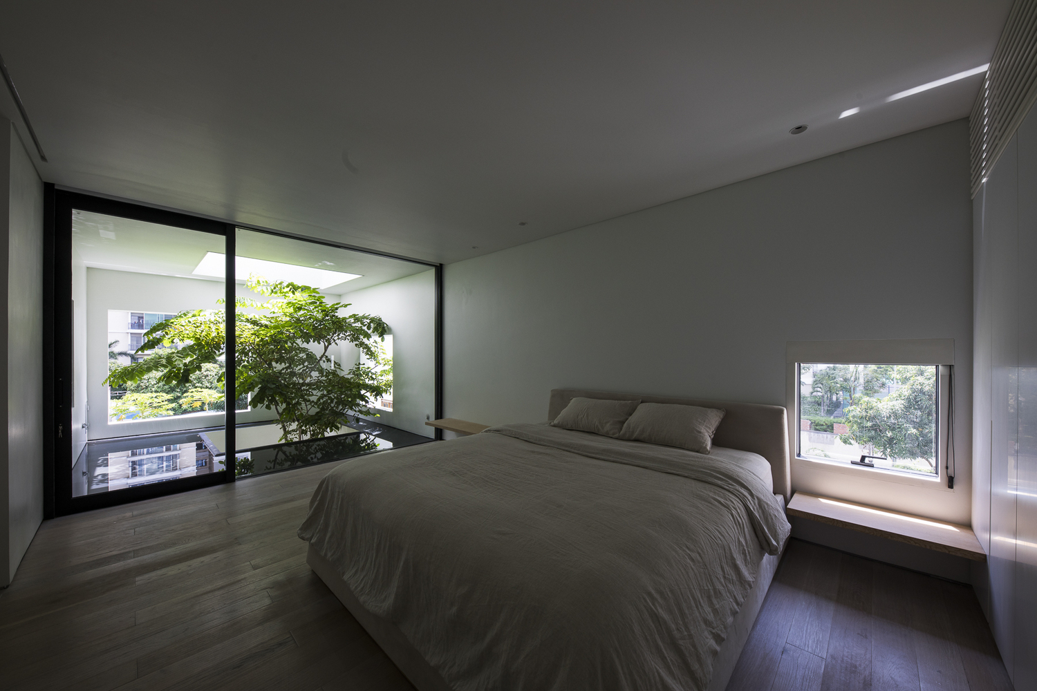 hình ảnh phòng ngủ với giường nệm màu trắng, sàn gỗ, cửa sổ kính, cửa mở ra thông tầng trồng cây xanh