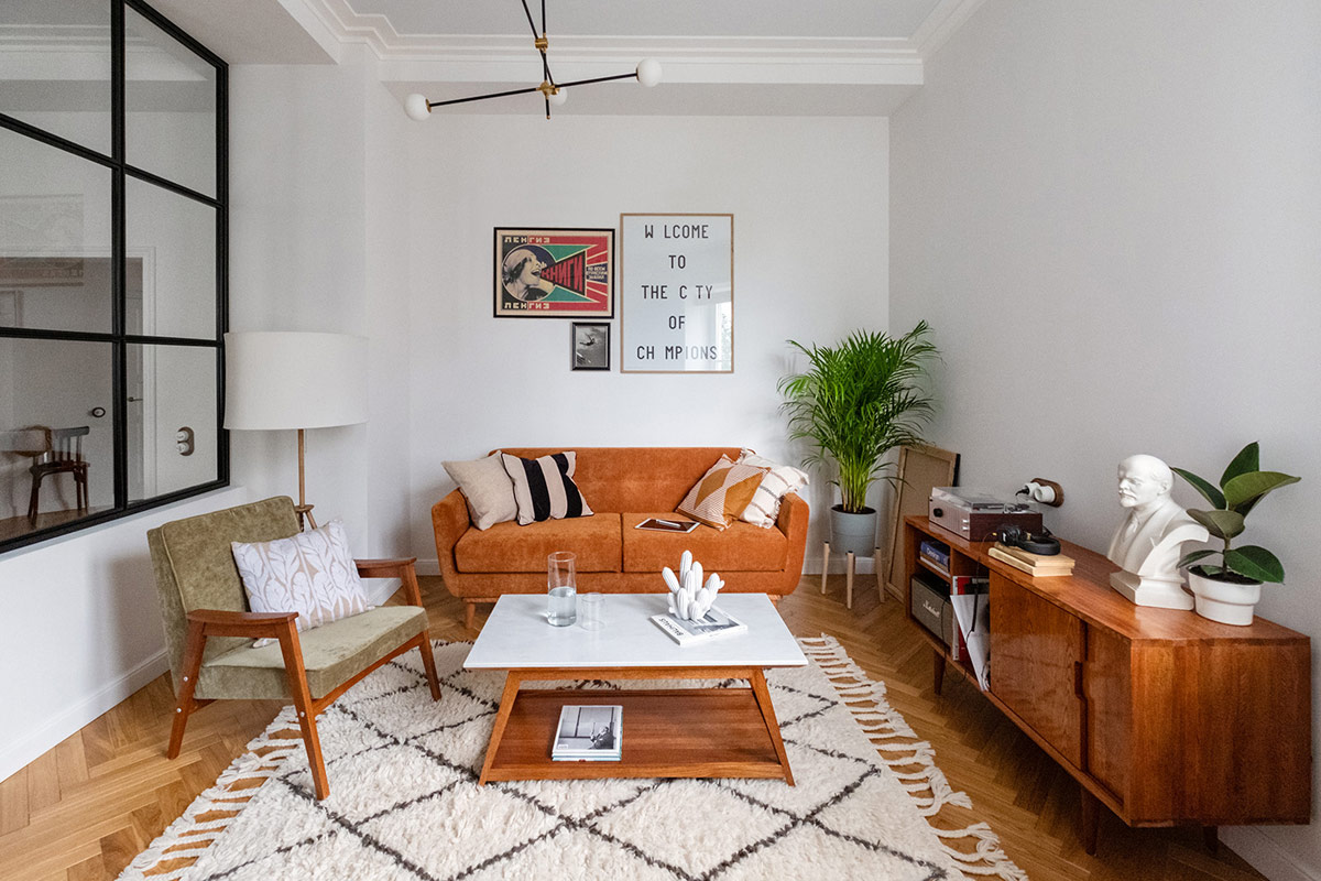 Trong phòng khách căn hộ 74m2, đồ nội thất màu nâu làm ấm không gian sống phong cách Mid-Century tông trắng chủ đạo. Thảm trải có tua rua tạo điểm nhấn sinh động.