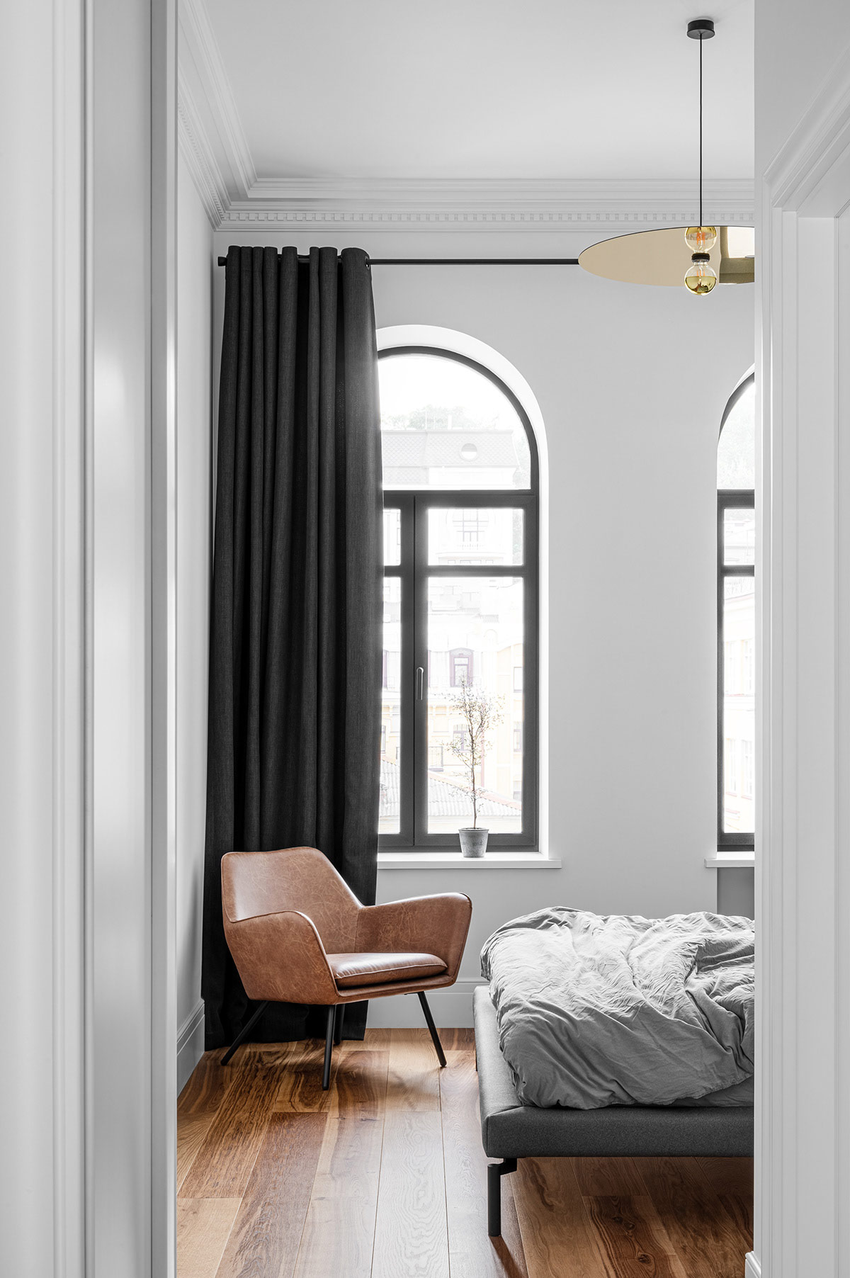 Ghế da màu nâu tương phản với rèm cửa và khung cửa sổ hình vòm màu đen. Đèn thả mặt dây chuyền màu vàng sáng bóng giúp làm ấm căn phòng về mặt thị giác.