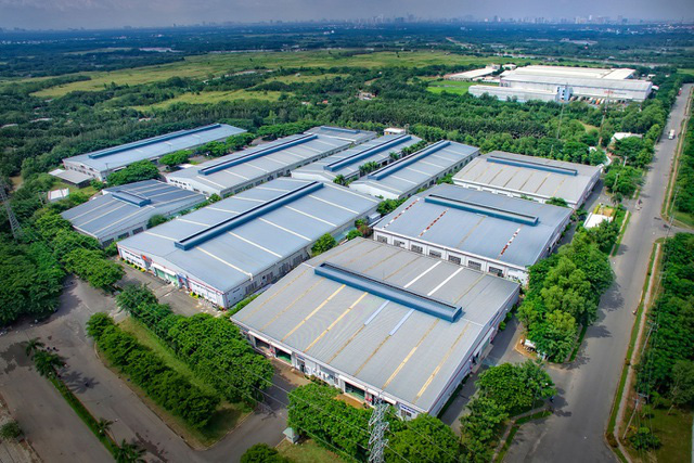 hình ảnh một khu công nghiệp nhìn từ trên cao với nhà xưởng màu xám trắng, xung quanh có nhiều cây cối, ruộng đồng