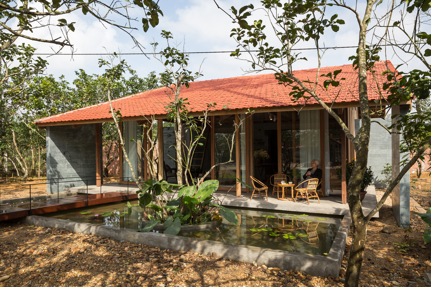 hình ảnh toàn cảnh ngôi nhà gỗ ở Huế với mái ngói đỏ, hồ sen nhỏ, bà cụ ngồi ở hiên nhà