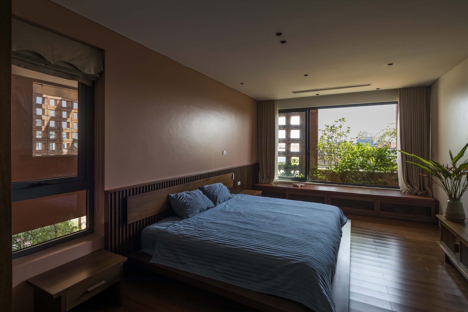 hình ảnh phòng ngủ rộng rãi, giường thấp, ga màu xanh than, cửa sổ kính rộng mở ra vườn cây xanh bên ngoài